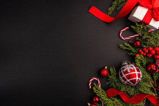 Festive pine branches decorated with red baubles, candy canes, and red ribbon on a black background, perfect for holiday-themed designs.