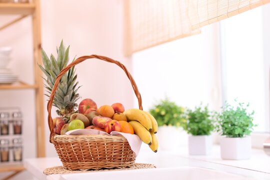 Different fresh fruits in wicker basket on countertop indoors, space for text