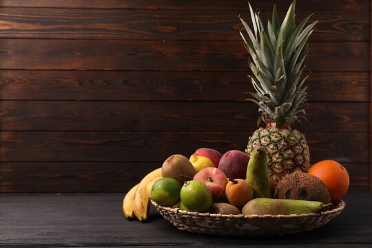 Different fresh fruits in wicker basket on black wooden table, space for text