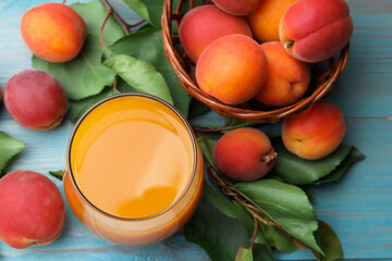 Apricot juice in glass, fresh fruits and leaves on light blue wooden table, above view © New Africa