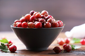 Fresh red gooseberries in bowl and green leaves on wooden table, closeup © New Africa