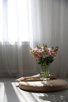 Bouquet of beautiful eustoma flowers in vase on wicker seat cushion near window indoors. Space for text