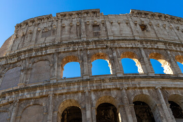 Obraz premium Famous Coliseum in Rome. Colosseum, or Coliseum. Part of the wall of an antique stone structure with arches. Italy, Europe. Famous touristic place in the world, Europe. Beautiful blue sky background.
