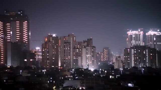 Panning night shot of lit up gurgaon cityscape with modern skyscrapers, high-rise construction, dense buildings, showing the rapid growth and urbanization of this city
