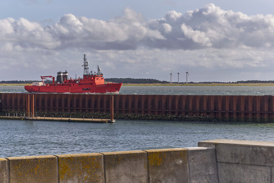 Esbjerg, Denmark - 27 July 2026: View of an Esvagt service vessel navigating the passage, with wind turbines on Fano island in the background under a cloudy sky.