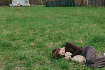 Naklejka premium Woman lying on grass cuddling a goat kid outdoors, showing countryside relaxation and gentle animal companionship. Warm natural light creates a calm, peaceful mood and sense of connection with nature.