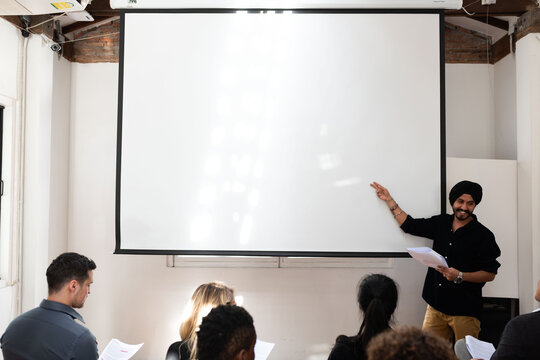 Man presenting to a small group in a bright room with a projector.