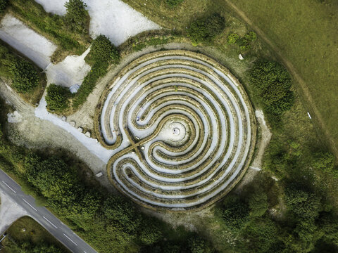 Aerial view of a circular stone labyrinth set within a grassy landscape near Colliford Lake, surrounded by trees and a nearby road in Cornwall, England, United Kingdom.