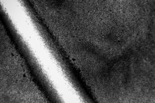 Dark, rough, granulated surface featuring a diagonal band of bright light and contrasting deep shadows, creating an abstract background