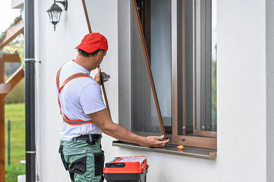 Worker installing mosquito wire screen on house window to protect from insects.