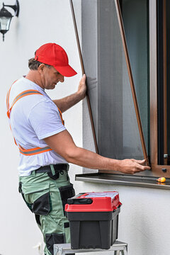Worker installing mosquito wire screen on house window to protect from insects.