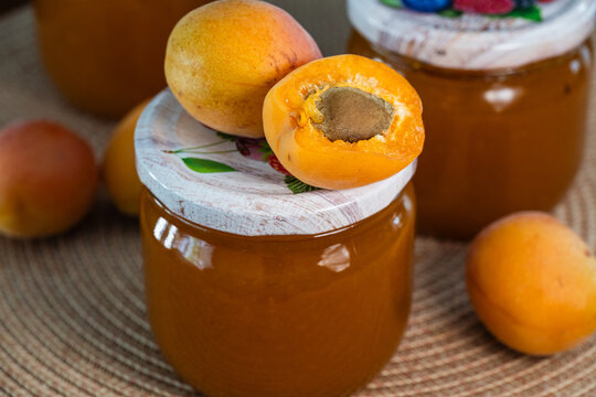 Fresh whole and halved apricots rest on the lid of a glass jar filled with homemade apricot jam.