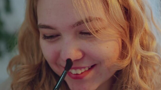 Close up of young woman applying makeup with soft lighting and calm expression. scene shows subject using various tools like brushes on her face focusing on texture detail in hair and skin