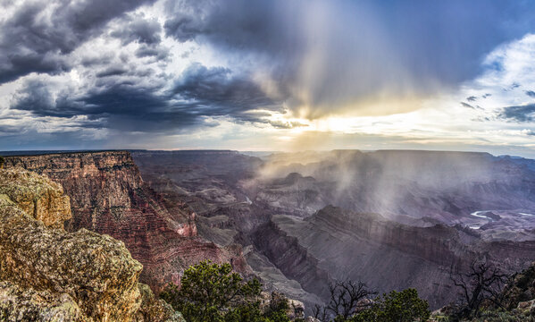 Aerial view of Grand Canyon with dramatic storm clouds and sun rays breaking through the rugged canyon walls in Coconino County, Arizona, United States.