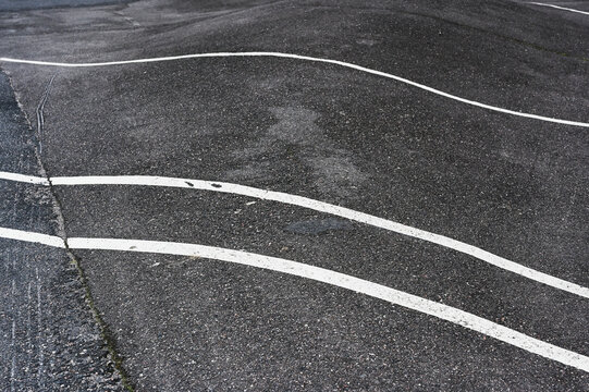 Abstract close-up of weathered asphalt marked with curved and irregular white road lines.