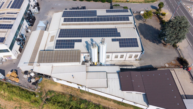 Aerial view of a specialty coatings manufacturing facility featuring extensive rooftop solar panels, industrial silos, and metal roofing in Milan, Lombardy, Italy.