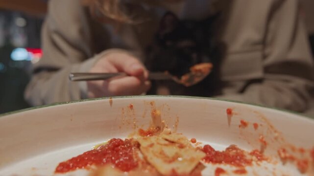Close up of woman eating pasta with tomato sauce using fork in indoor setting. focus is on hand utensil and food texture details like red chunky tomatoes spread over flat pasta sheets