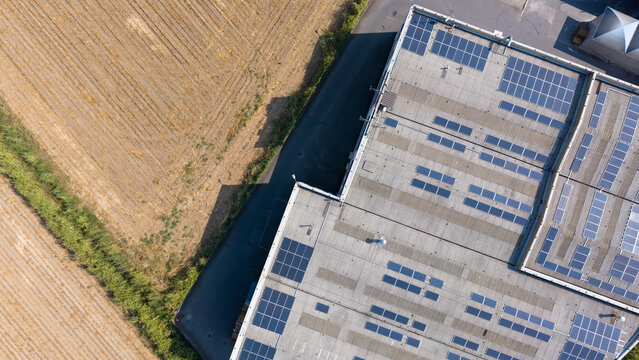 Aerial view of a specialty coatings manufacturing facility featuring extensive rooftop solar panels adjacent to agricultural fields in Milan, Lombardy, Italy.