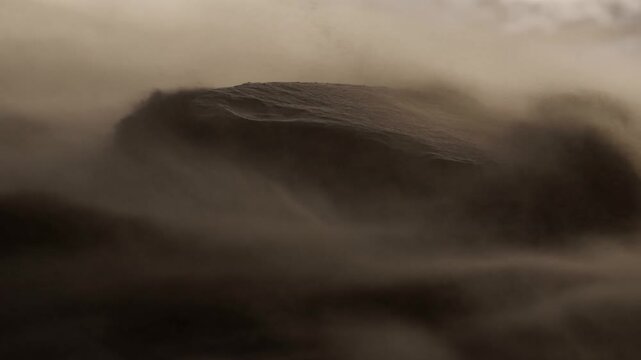 Rock surrounded by blowing dust in a barren desert landscape during a sandstorm