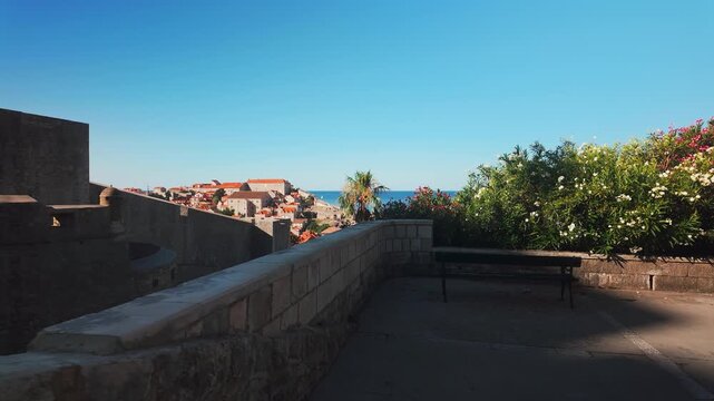 Tourist perspective walking down stone steps toward historic Dubrovnik, Croatia, passing ancient city walls and oleander bushes with scenic views of the Old Town.