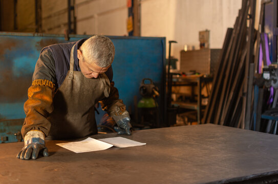 Industrial welder inspecting technical drawing at workshop workbench