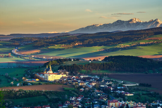 Aerial view of Spisska Kapitula with its historic cathedral, surrounded by green fields and rolling hills, with the High Tatras mountains on the horizon in Levoca, Presovsky kraj, Slovakia.