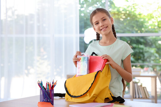 Girl packing her backpack for school at wooden table indoors