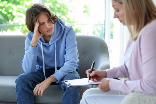 Teenage boy having appointment with psychologist in office, selective focus