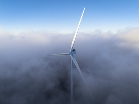 Aerial view of Windpark Freilanderalm rising above a thick layer of clouds with a clear blue sky above in Hebalm, Styria, Austria.