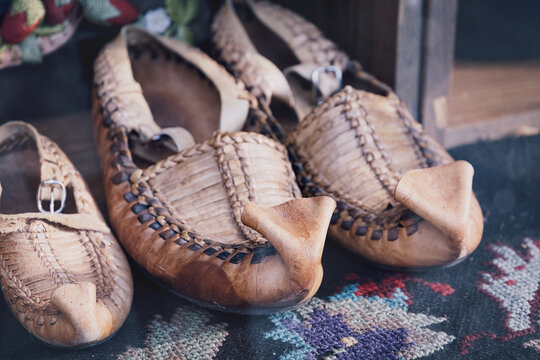 Traditional Serbian opanci, handmade leather footwear, displayed on a colorful patterned folk carpet, representing Balkan culture