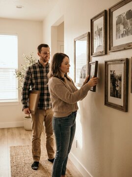 Happy young couple decorating their home hallway by hanging wooden framed family pictures on the wall