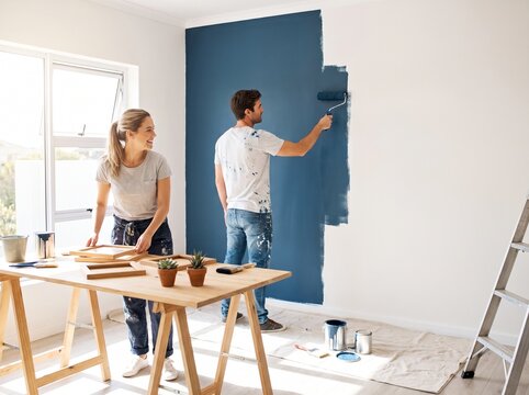 Happy young couple renovating and decorating their home painting a wall blue together