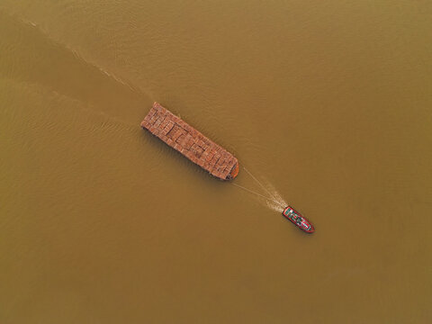Aerial view of a tugboat towing a large barge loaded with timber logs along the Mahakam River in Kota Samarinda, Kalimantan Timur, Indonesia.