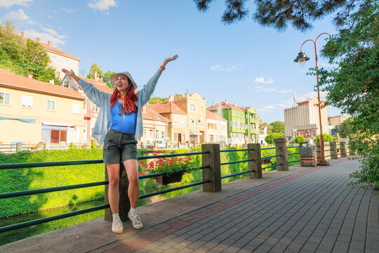 Woman enjoying carefree summer city break in Knjazevac, Serbia, smiling by the historic canal promenade with arms outstretched