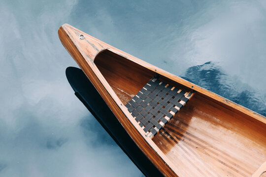 Wooden canoe floating on tranquil lake water, creating a serene outdoor scene, reflecting sky and promoting adventure and peace