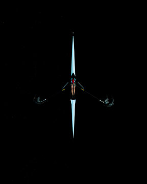 Aerial view of a single rower in a sculling boat gliding across dark water in Poland.