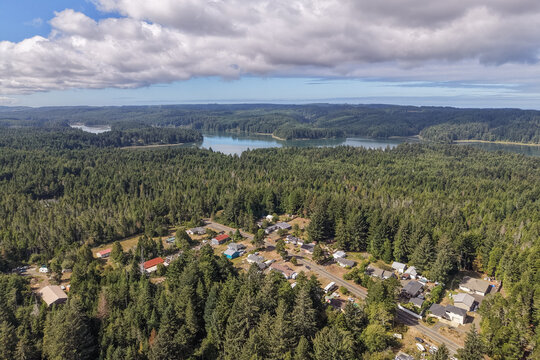 Aerial view of the Crown Point neighborhood surrounded by dense evergreen forests and a calm lake under a cloudy sky in Charleston, Oregon, United States.