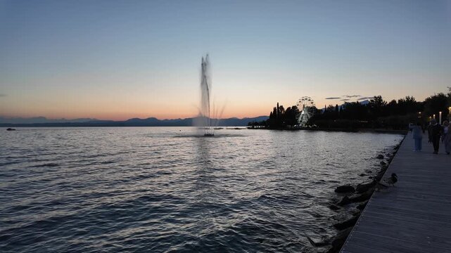 Bardolino, Italy - May 17, 2026 - Sunset over lake with fountain and Ferris wheel on the shore