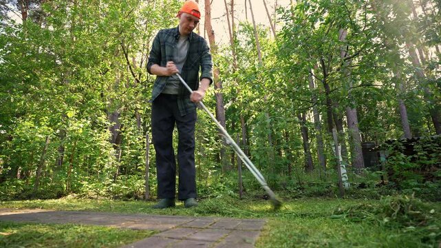Man rake grass in backyard garden during autumn work
