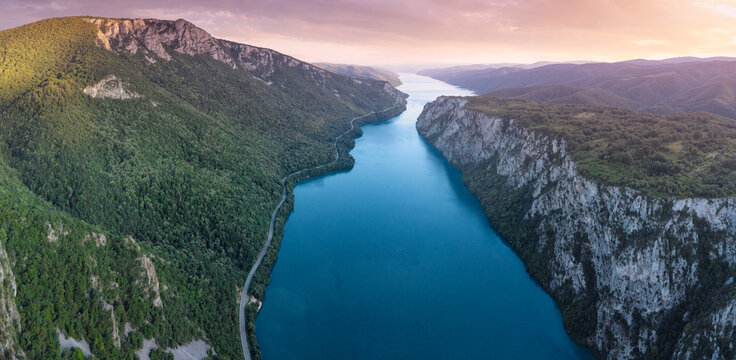 Aerial view of the Danube river winding through the dramatic Iron Gates gorge, surrounded by lush forested mountains at sunset
