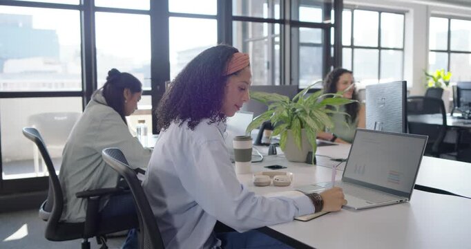 Diverse women at office African American woman jotting notes at laptop, camera catching eye