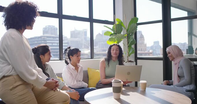 Diverse female team at office, presenter opening laptop, sharing slides on lap, hijab woman leaning