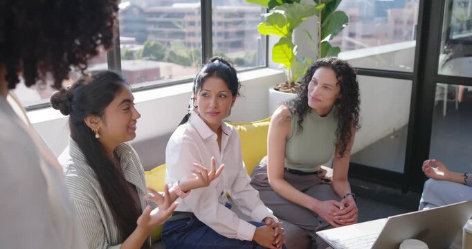 Female team sitting at office listening, sharing ideas as standing speaker gesturing at laptop