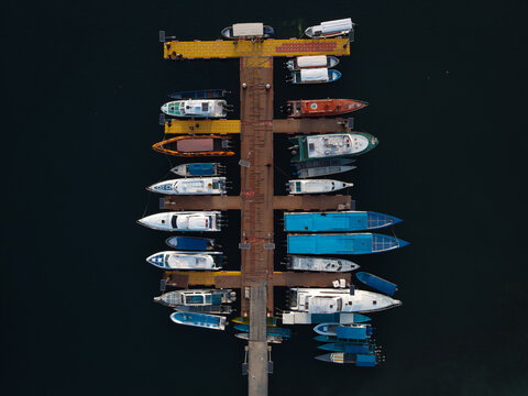 Aerial view of Waisai Harbour with various boats and yachts moored at the wooden pier in the clear tropical waters in Raja Ampat, Papua Barat Daya, Indonesia.