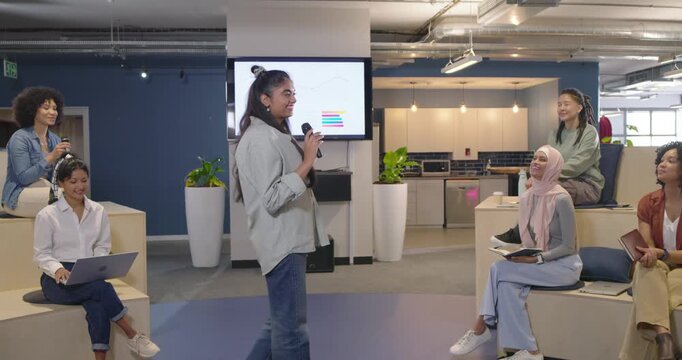 Diverse team in lounge watching Nonbinary speaker starting presentation, showing charts on screen