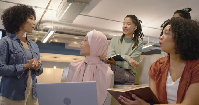 Diverse coworkers moving closer, standing speaker gesturing, hijab woman typing on laptop