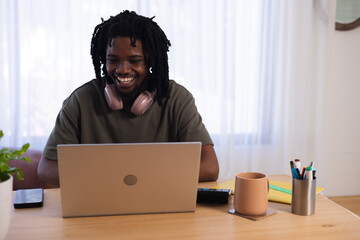 Adult man sitting at wooden table working on laptop wearing pink headphones, phone and mug visible © WavebreakMediaMicro