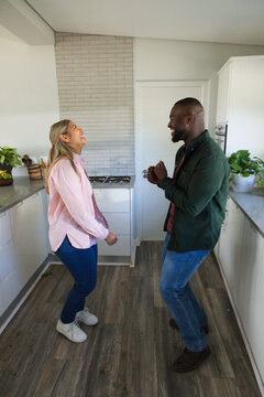 African American couple laughing and gesturing in galley kitchen by gas cooktop, fruit basket