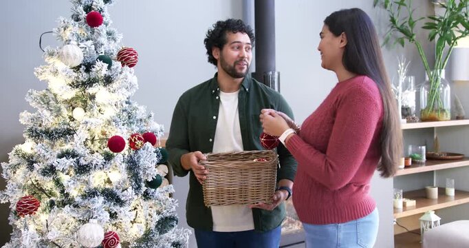 African American couple decorating tree for holiday, man holding basket while woman hanging baubles