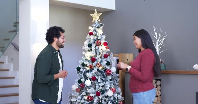 African American couple decorating Xmas tree for holiday at home woman showing ornament man smiling